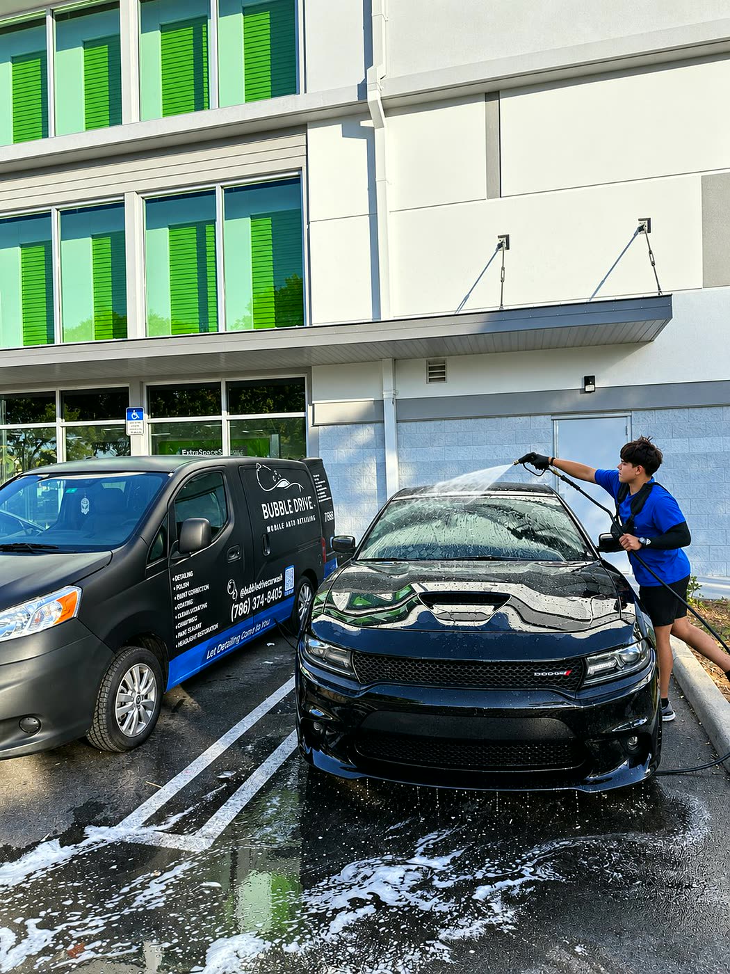 Technician pressure washing Dodge next to Bubble Drive van in Miami