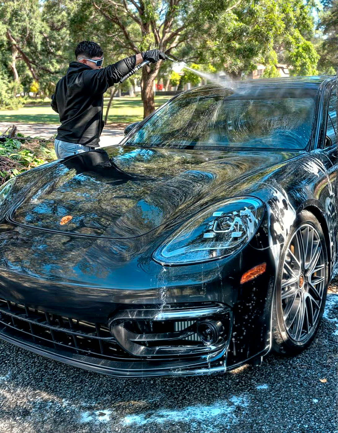Technician pressure washing a black Porsche during exterior detailing in Miami
